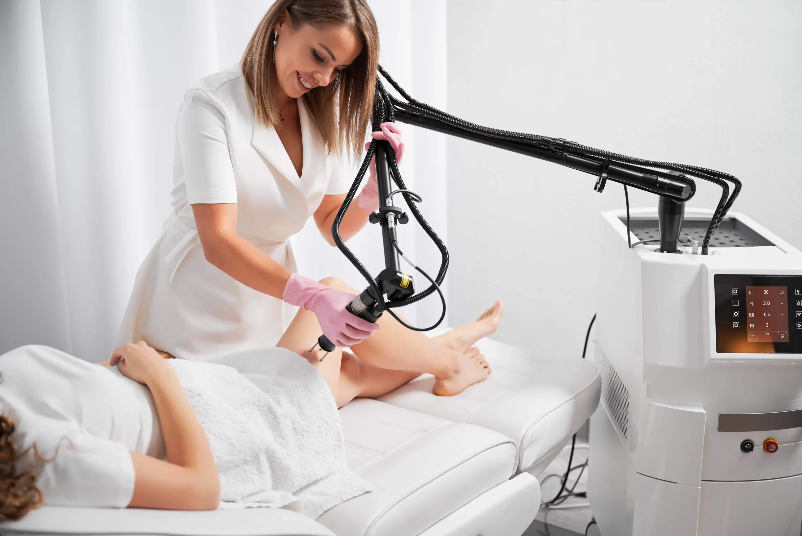 A provider uses a CO₂ laser handpiece on a patient’s legs during a skin resurfacing treatment for Enhanced Wellness in Derby Kansas. The treatment room shows the laser console and the patient lying on a white treatment bed.