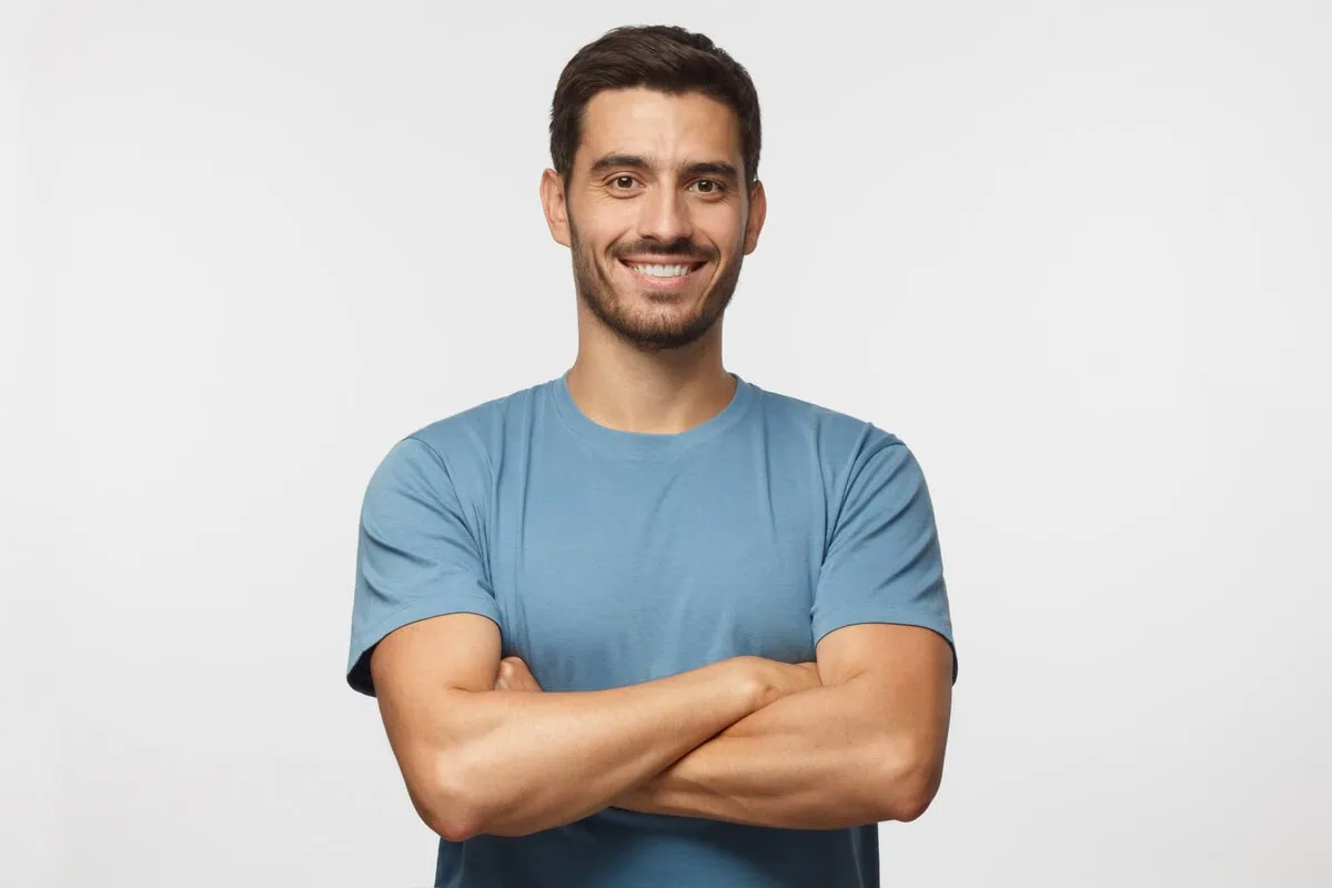 A smiling man stands with arms crossed against a plain background to represent confidence and wellness for Enhanced Wellness in Derby, Kansas. His relaxed posture highlights a positive treatment outcome.